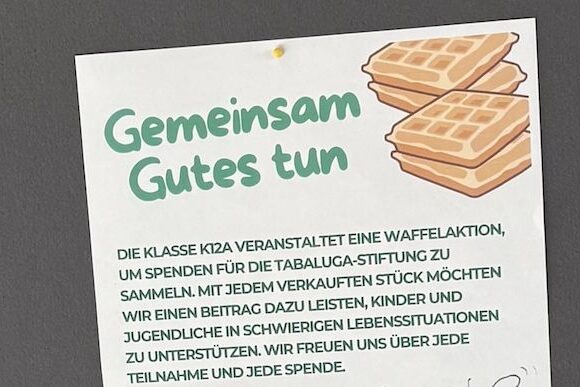 Foto Stellwand_bearbeitet Auf einem Flyer mit illustrierten Waffeln in der Ecke steht "Gemeinsam Gutes tun". Er kündigt einen Waffelverkauf der Klasse K12A an, um Spenden für die Tabaluga-Stiftung zu sammeln, die Kinder und Jugendliche in Not unterstützt.