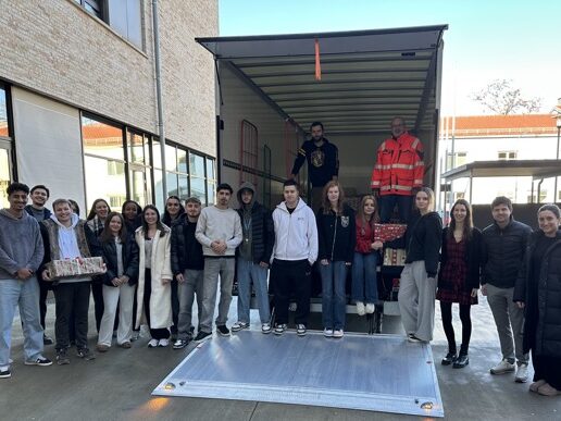 Johann. Weihn.t. 600×387 Eine Gruppe von Menschen steht draußen neben einem Lastwagen mit offener Ladefläche. Einige halten in Geschenkpapier verpackte Kartons in der Hand, und ein paar Leute stehen im Inneren des Lastwagens. Die Szene scheint eine Spenden- oder Geschenkübergabe zu sein.