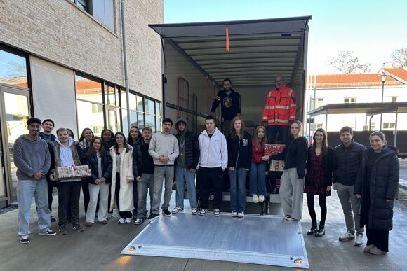 Johann. Weihn.t. 600×387 Eine Gruppe von Menschen steht draußen neben einem Lastwagen mit offener Ladefläche. Einige halten in Geschenkpapier verpackte Kartons in der Hand, und ein paar Leute stehen im Inneren des Lastwagens. Die Szene scheint eine Spenden- oder Geschenkübergabe zu sein.