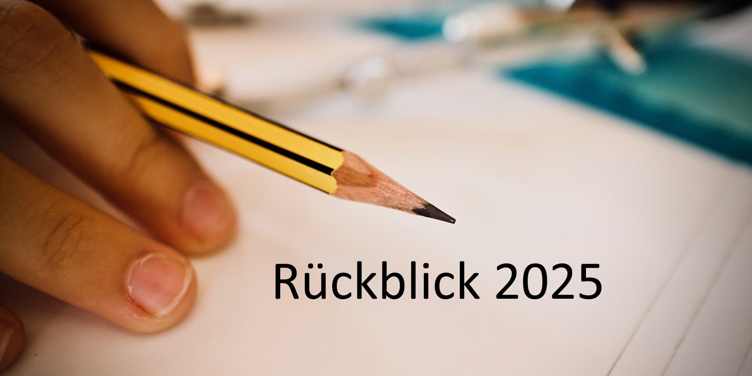 Rückblick 2025 Eine Hand, die einen gelben Bleistift über ein leeres Papier hält, mit dem deutschen Text Rückblick 2025 in der Mitte. Die Zeichenwerkzeuge sind im Hintergrund verschwommen.